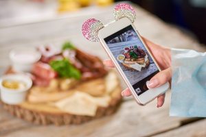 Woman taking a photo of grilled sausages. Woman hand using smartphone to take a photo of dish. Woman taking a photo of delicious food with smartphone at restaurant.